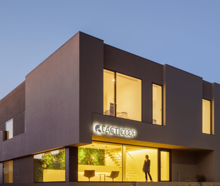 Vista geral do edifício Lacticoop ao entardecer com iluminação interior e letreiro luminoso - obra Contracta Engenharia, Aveiro