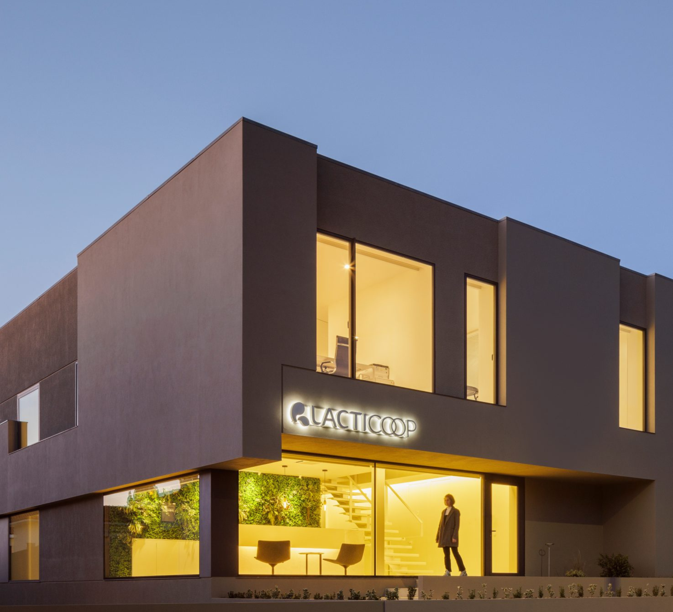 Vista geral do edifício Lacticoop ao entardecer com iluminação interior e letreiro luminoso - obra Contracta Engenharia, Aveiro